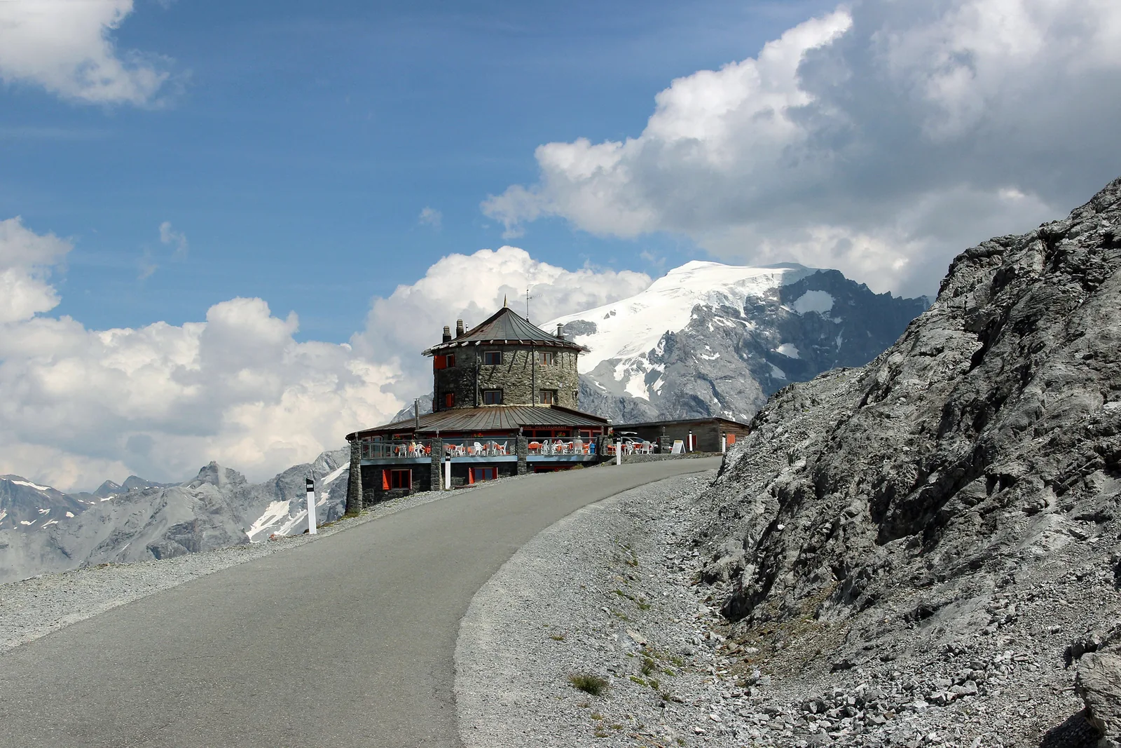 The road at the summit of the Stelvio Pass with the Tibet hut, the glaciated Ortler massif behind