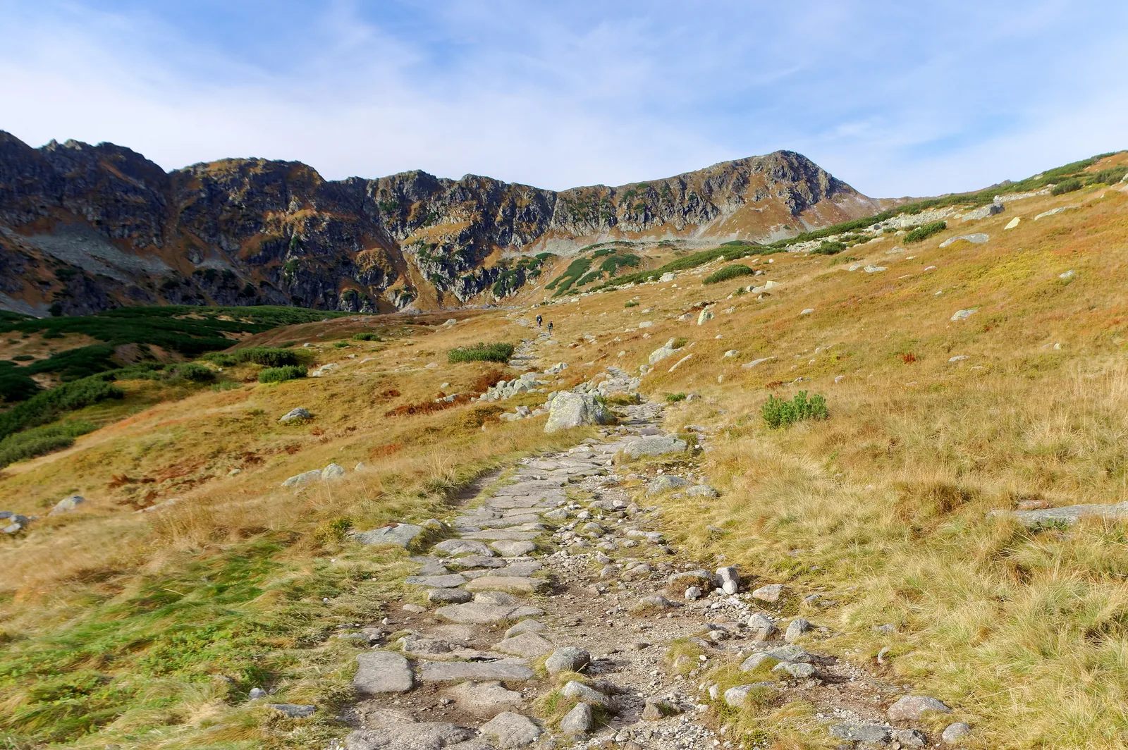 The Valley of Five Polish Ponds in Tatra National Park in October: a stone path through brown grass, rocky ridges behind