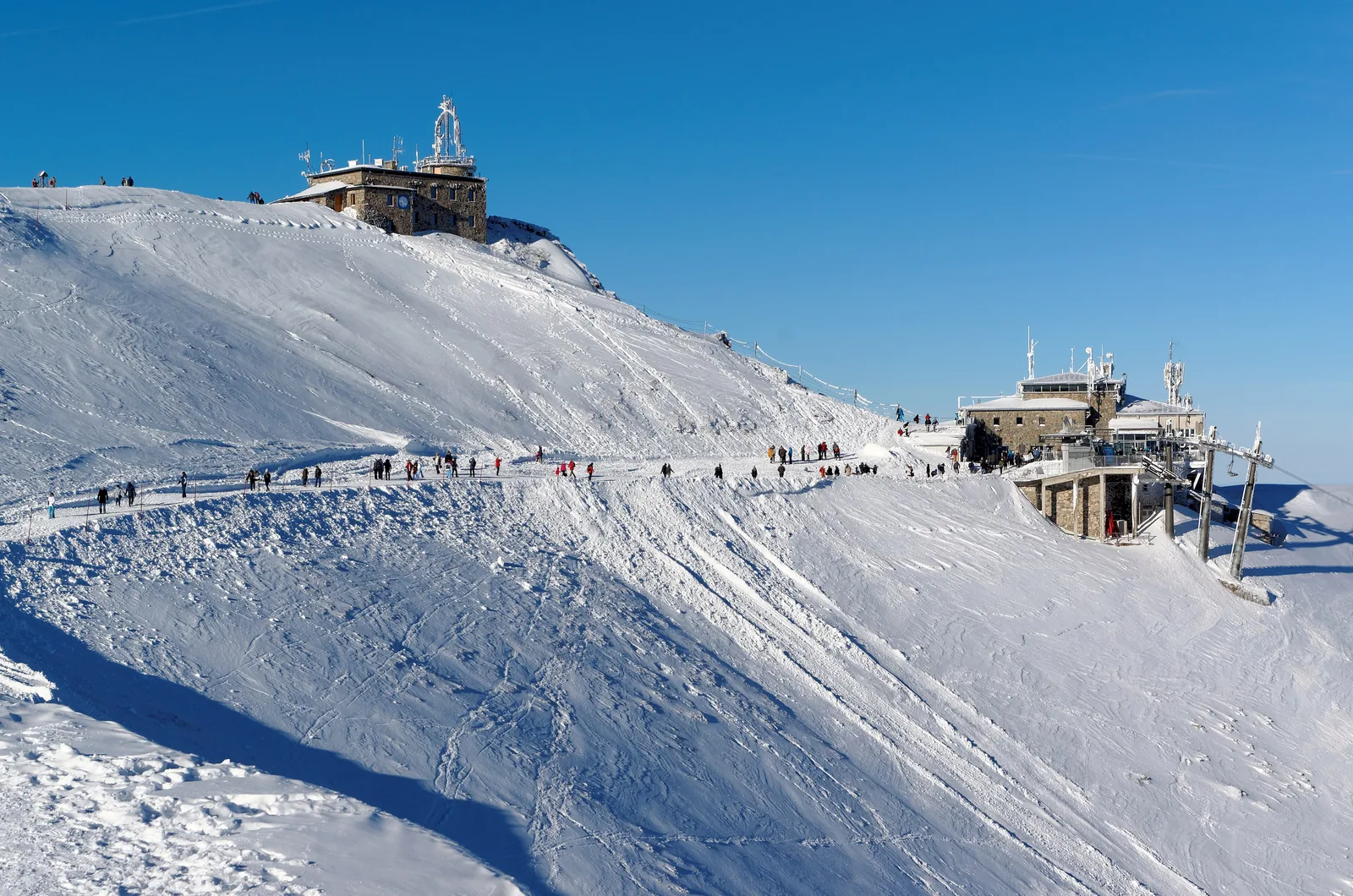 The weather observatory on the summit of Kasprowy Wierch and the cable car top station in snow, hikers on the ridge