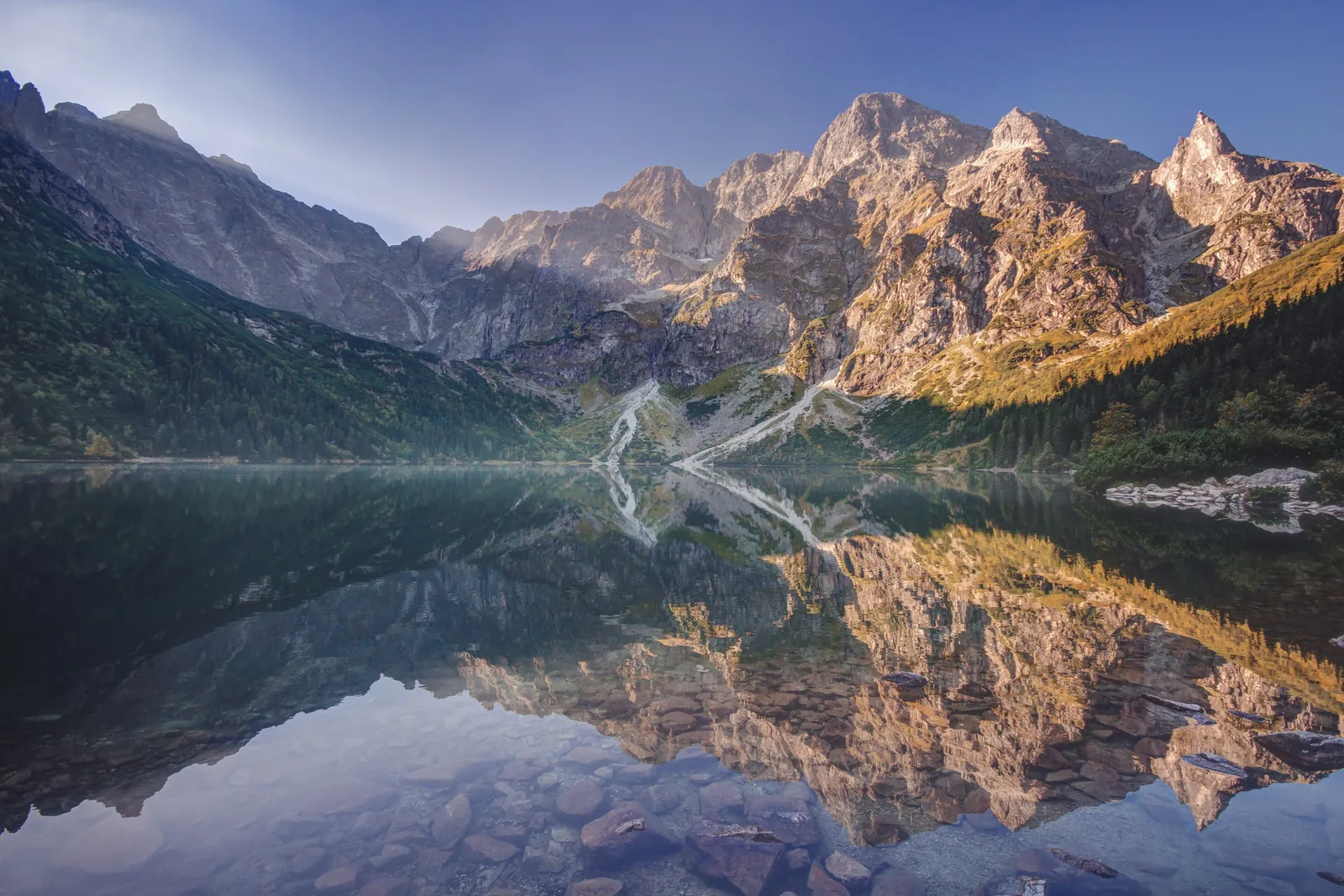 Morskie Oko in Tatra National Park in the morning: the peaks above the lake reflected in the still water, wooded slopes on the right