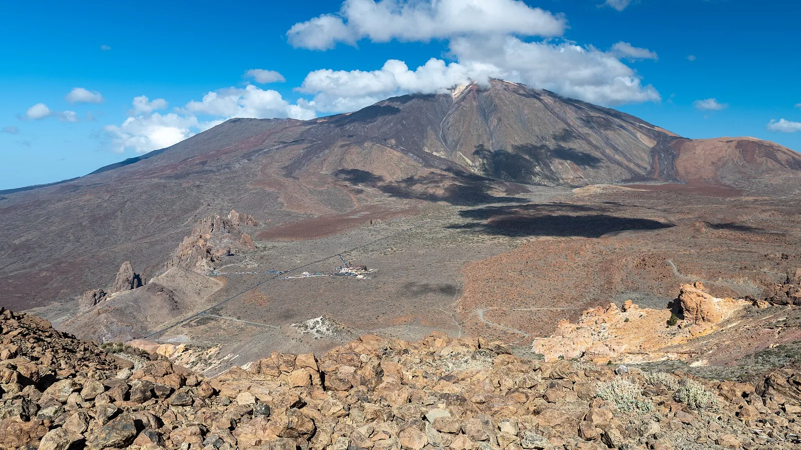 From the slope of Montaña Guajara in Teide National Park across the caldera floor and the rock spires of the Roques de García to Teide, with a cloud above the summit