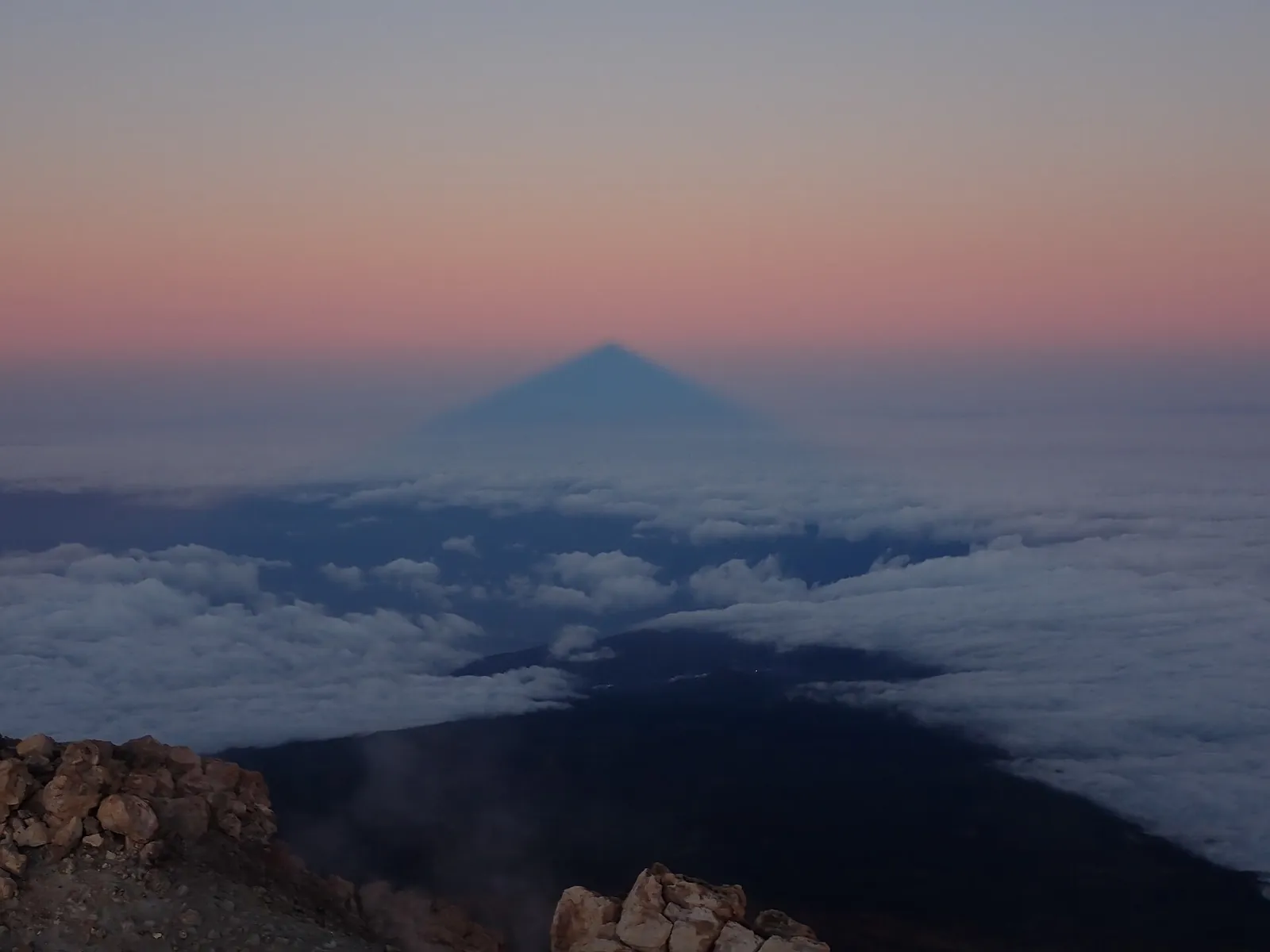 At sunrise in Teide National Park the triangular shadow of Teide falls across the sea of clouds to the pink horizon