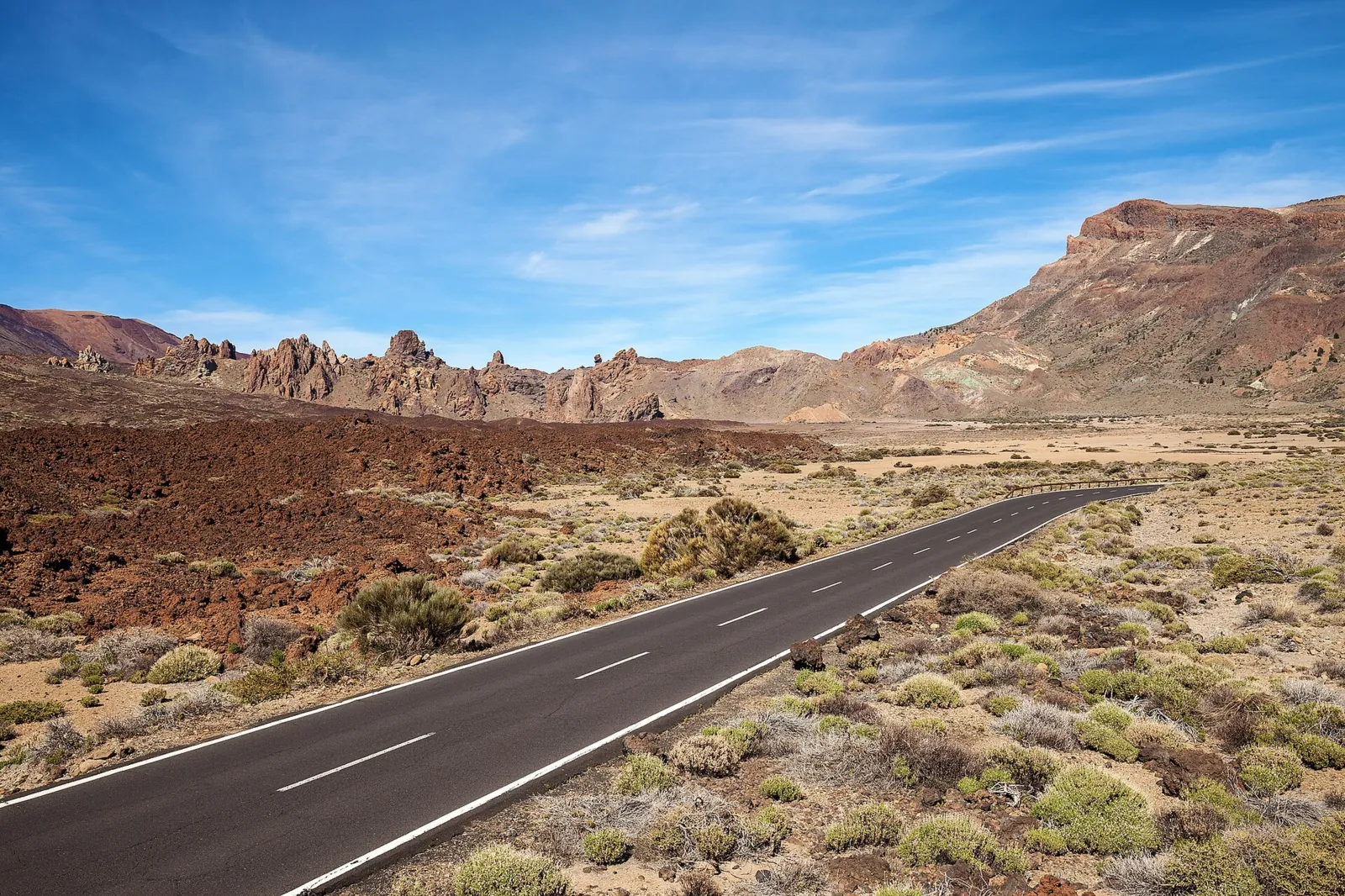 The TF-21 runs through broom bushes and lava fields in Teide National Park, with the rock spires of the Roques de García and the caldera wall behind