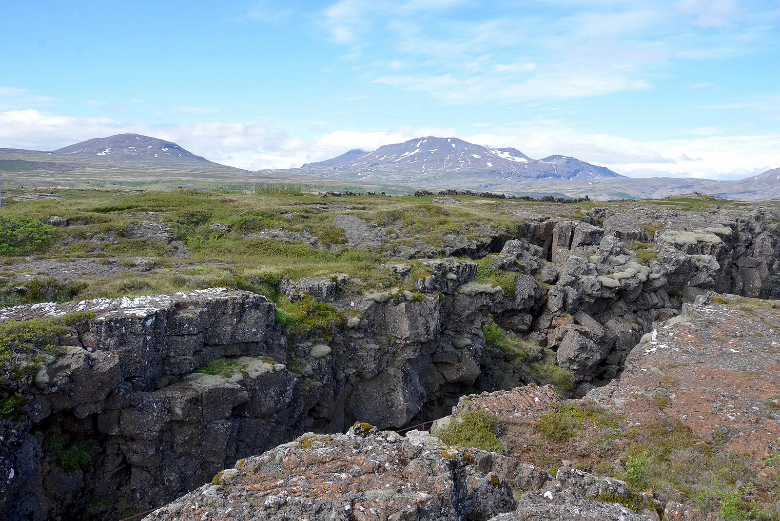 Almannagjá in Þingvellir National Park: a moss-covered fissure in the lava field, mountains with patches of snow behind