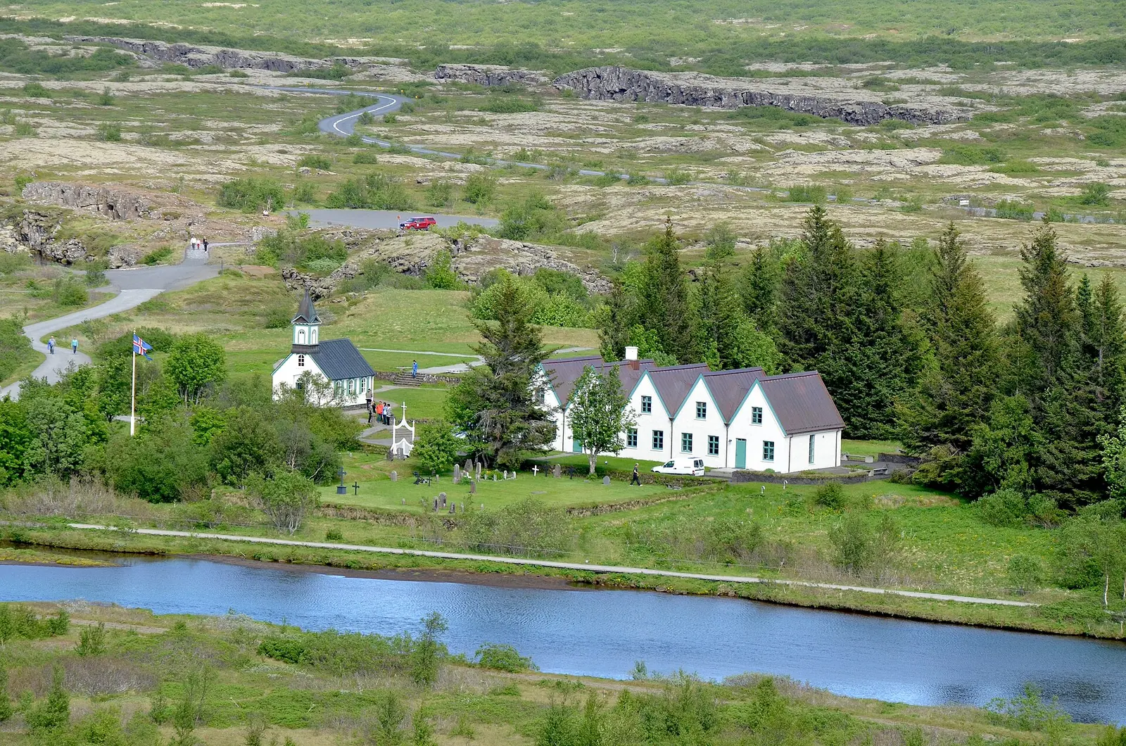 The white Þingvallakirkja and the gables of the Þingvallabær farmhouse in Þingvellir National Park, the Öxará in front, the lava plain behind