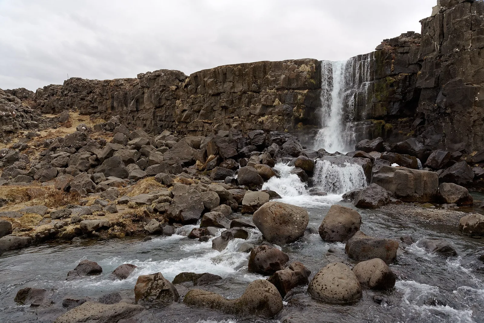 Öxarárfoss in Þingvellir National Park drops over a dark basalt edge into a pool full of round boulders