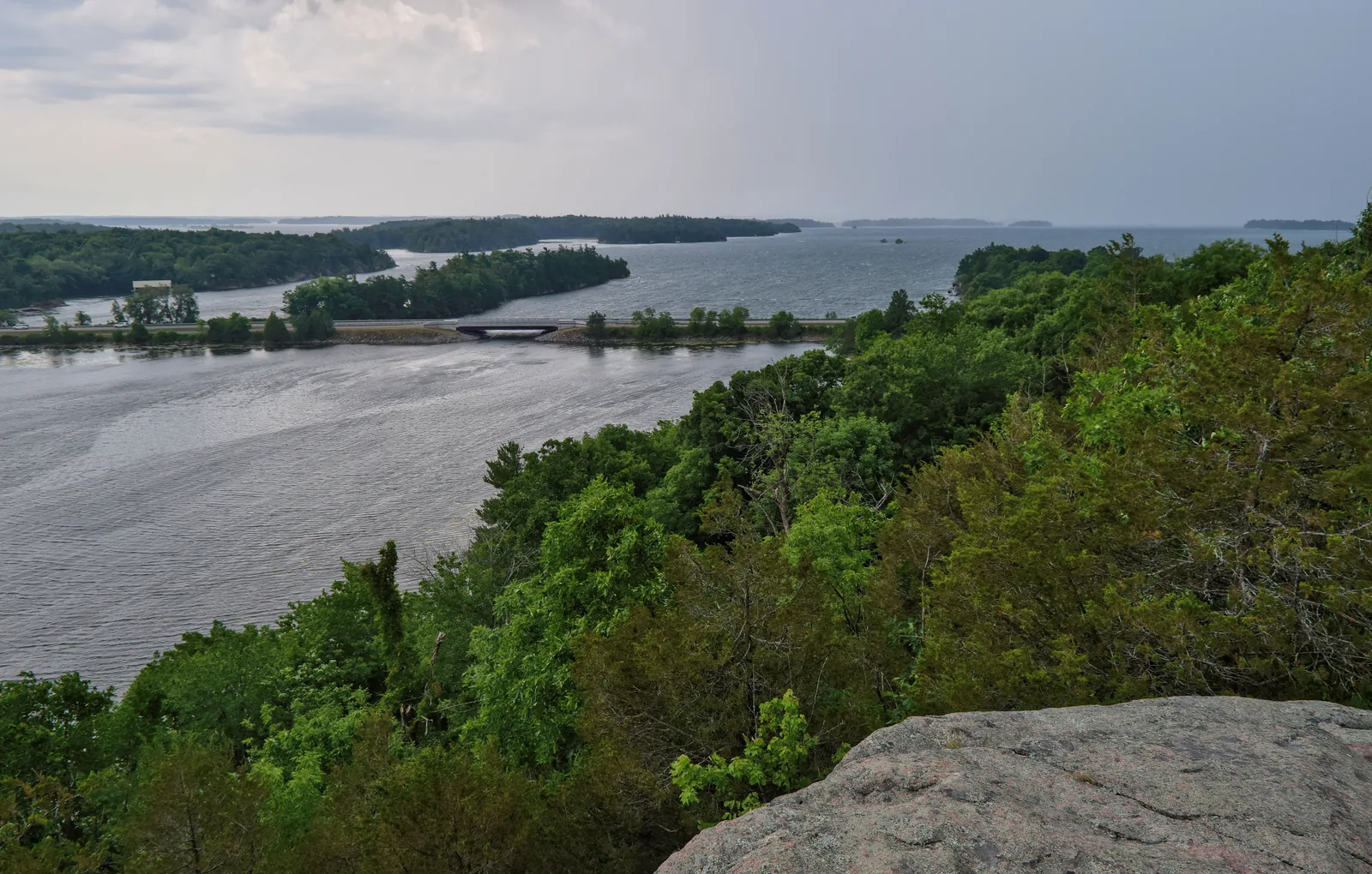 View from a granite rock over forested shores to the wide river with low islands under a cloudy sky