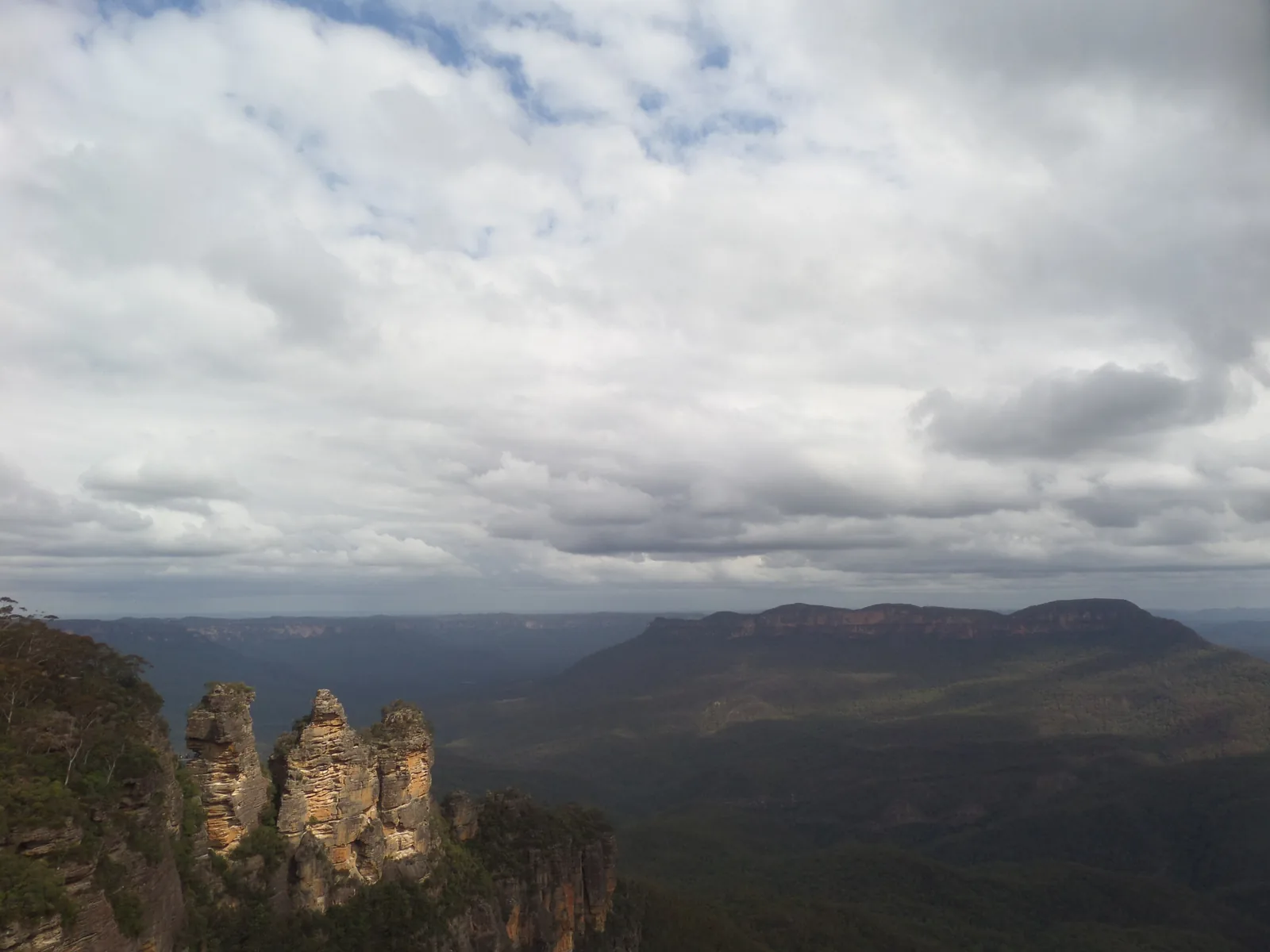 The Three Sisters in Blue Mountains National Park under grey clouds, with the Jamison Valley and the flat-topped Mount Solitary behind