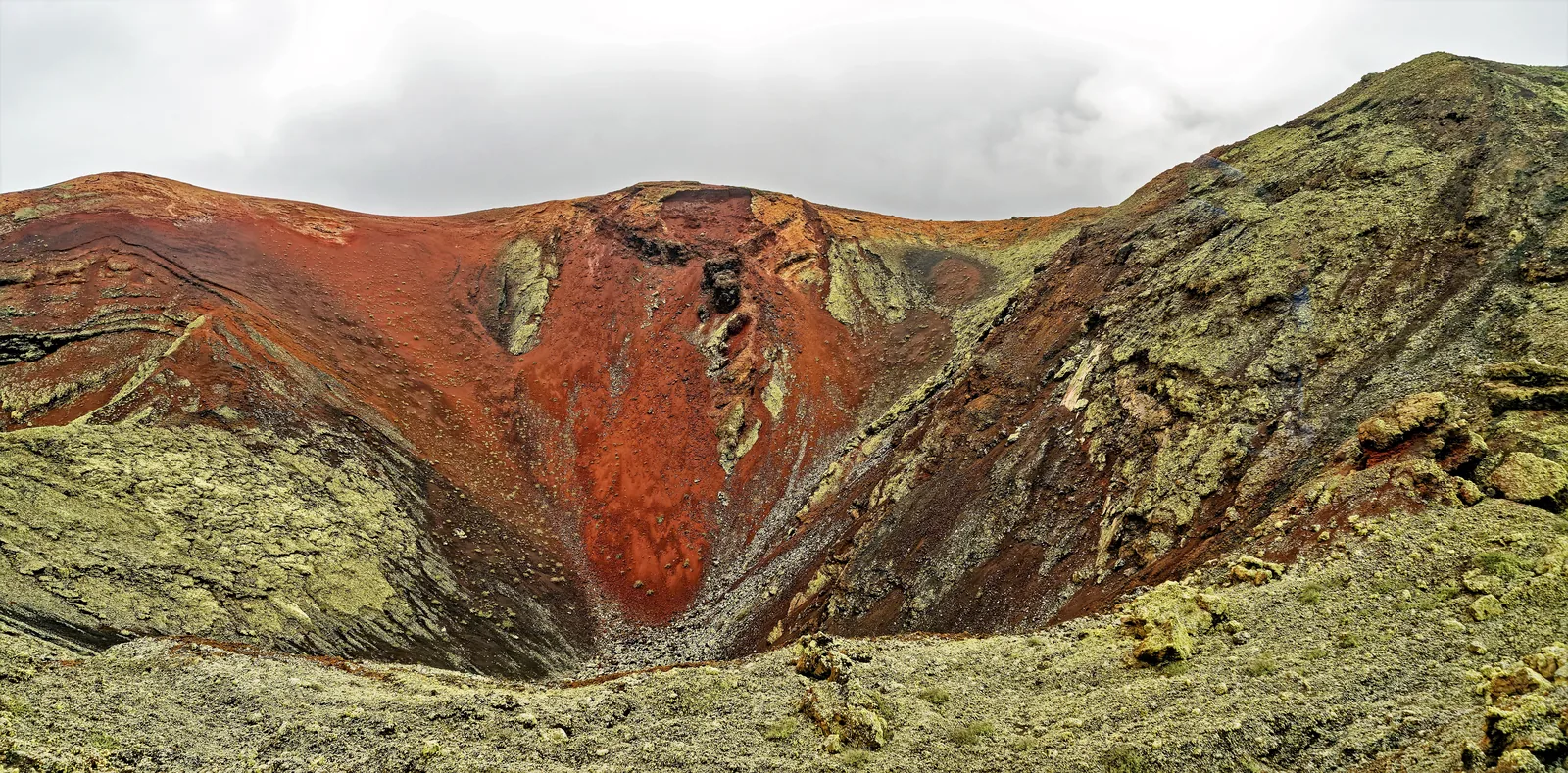 A crater coloured red and green in the core of the Montañas del Fuego in Timanfaya National Park, seen from the bus route