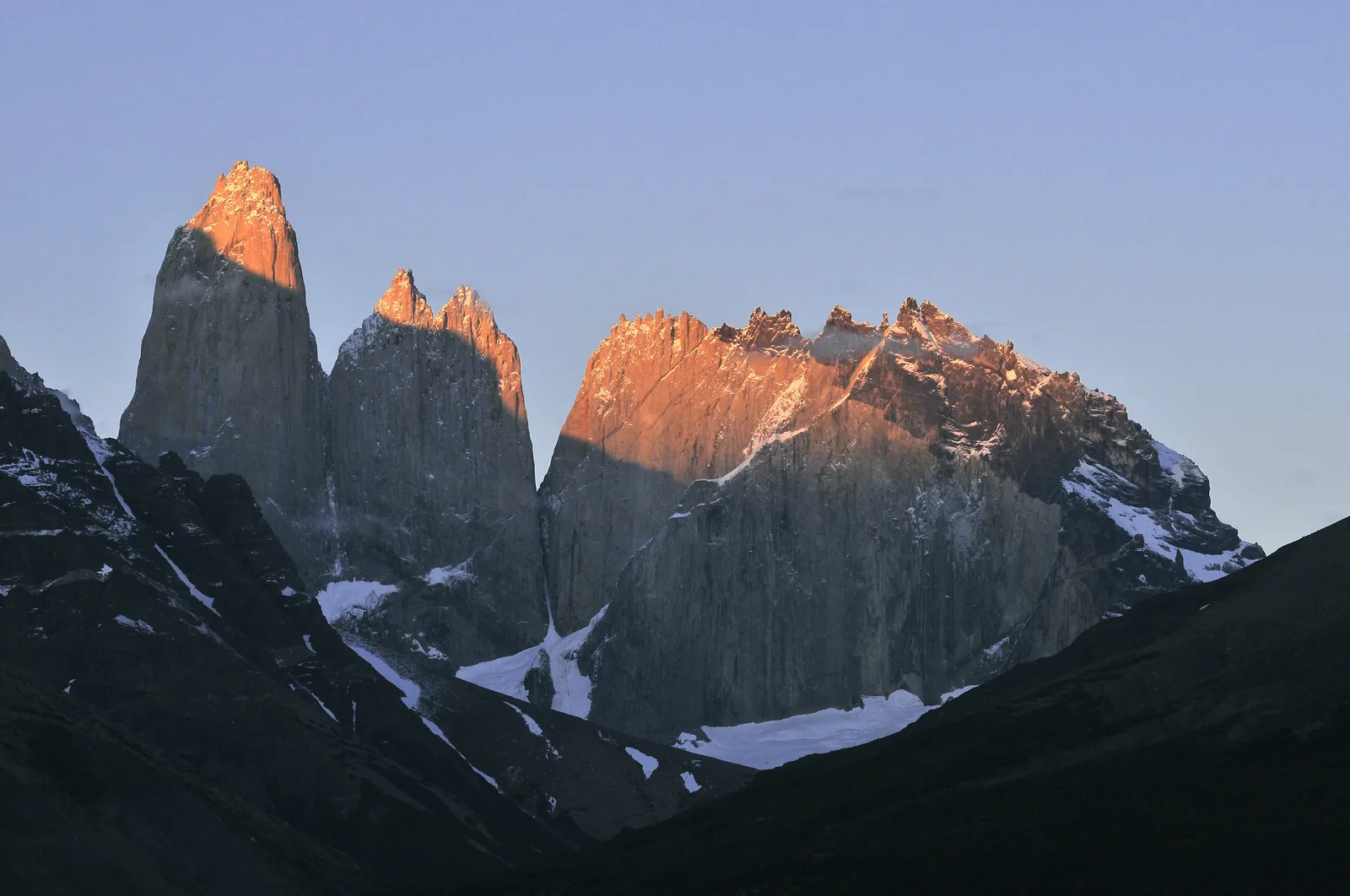 The Torres del Paine in Torres del Paine National Park at sunrise: the granite towers and peaks glow orange above dark slopes with patches of snow