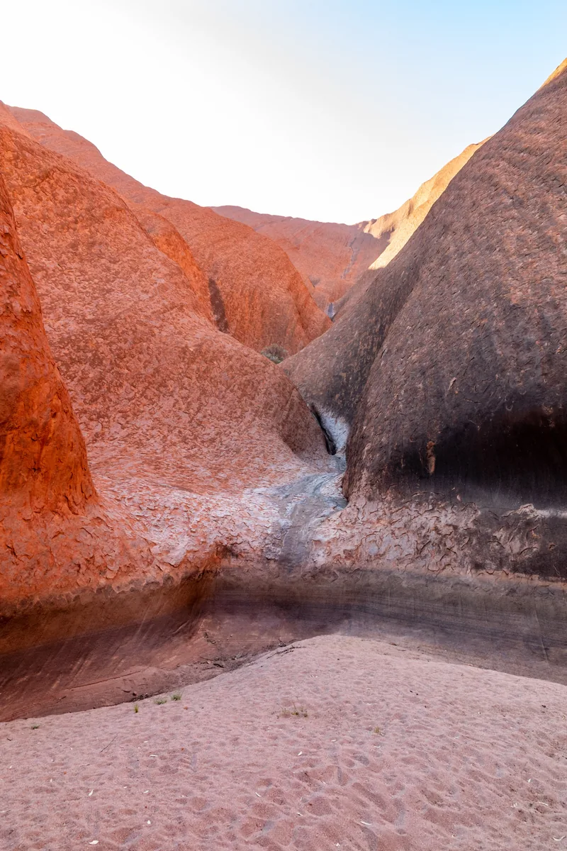 Mutitjulu Waterhole at Uluru in Uluṟu-Kata Tjuṯa National Park: a rock channel between two reddish rock walls runs into a pool, with pale sand in front