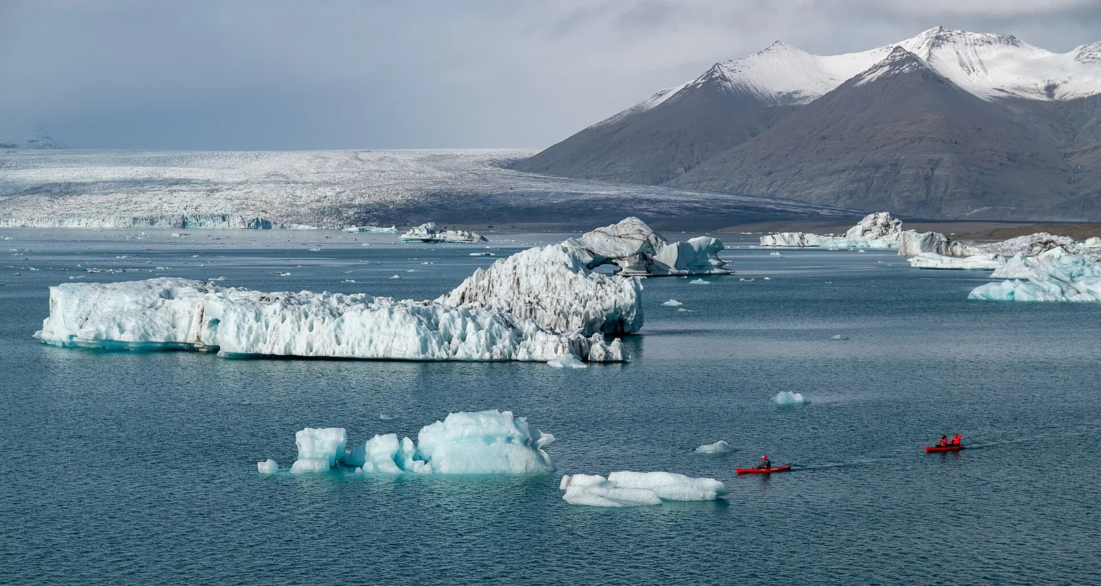 Kayaks among icebergs on Jökulsárlón in Vatnajökull National Park, the glacier snout and snow-covered mountains behind