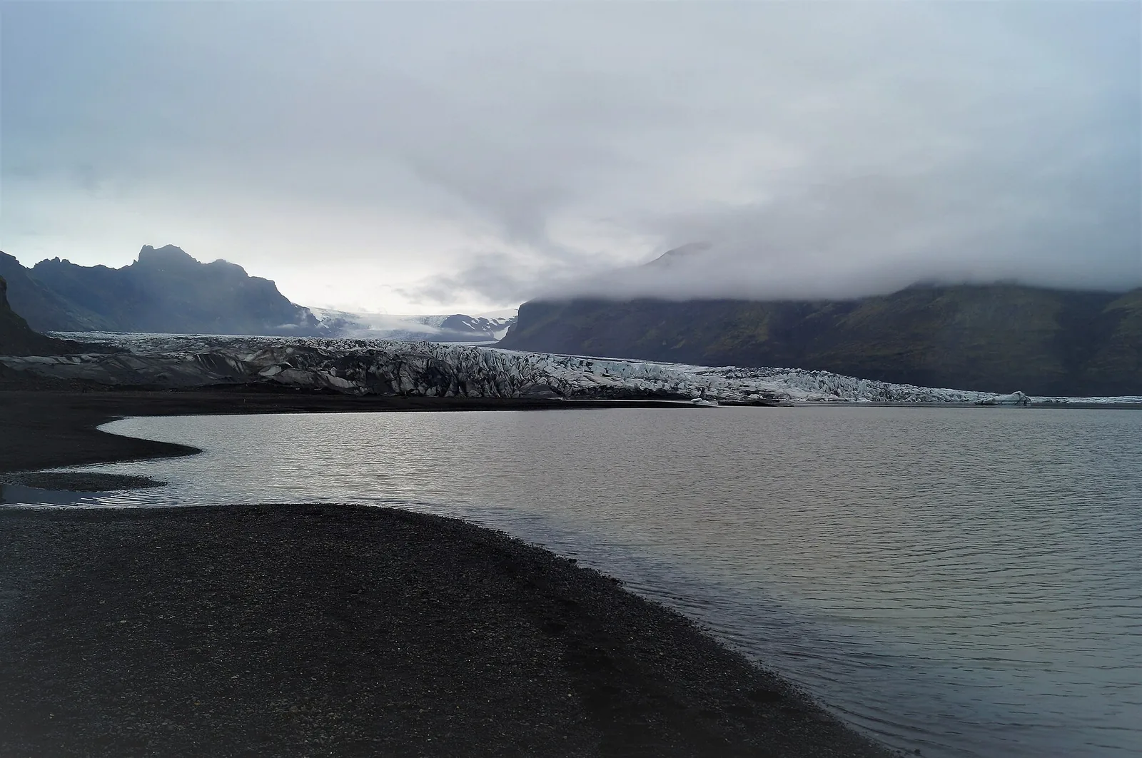 The snout of Skaftafellsjökull in Vatnajökull National Park behind a meltwater lake, dark sand in the foreground