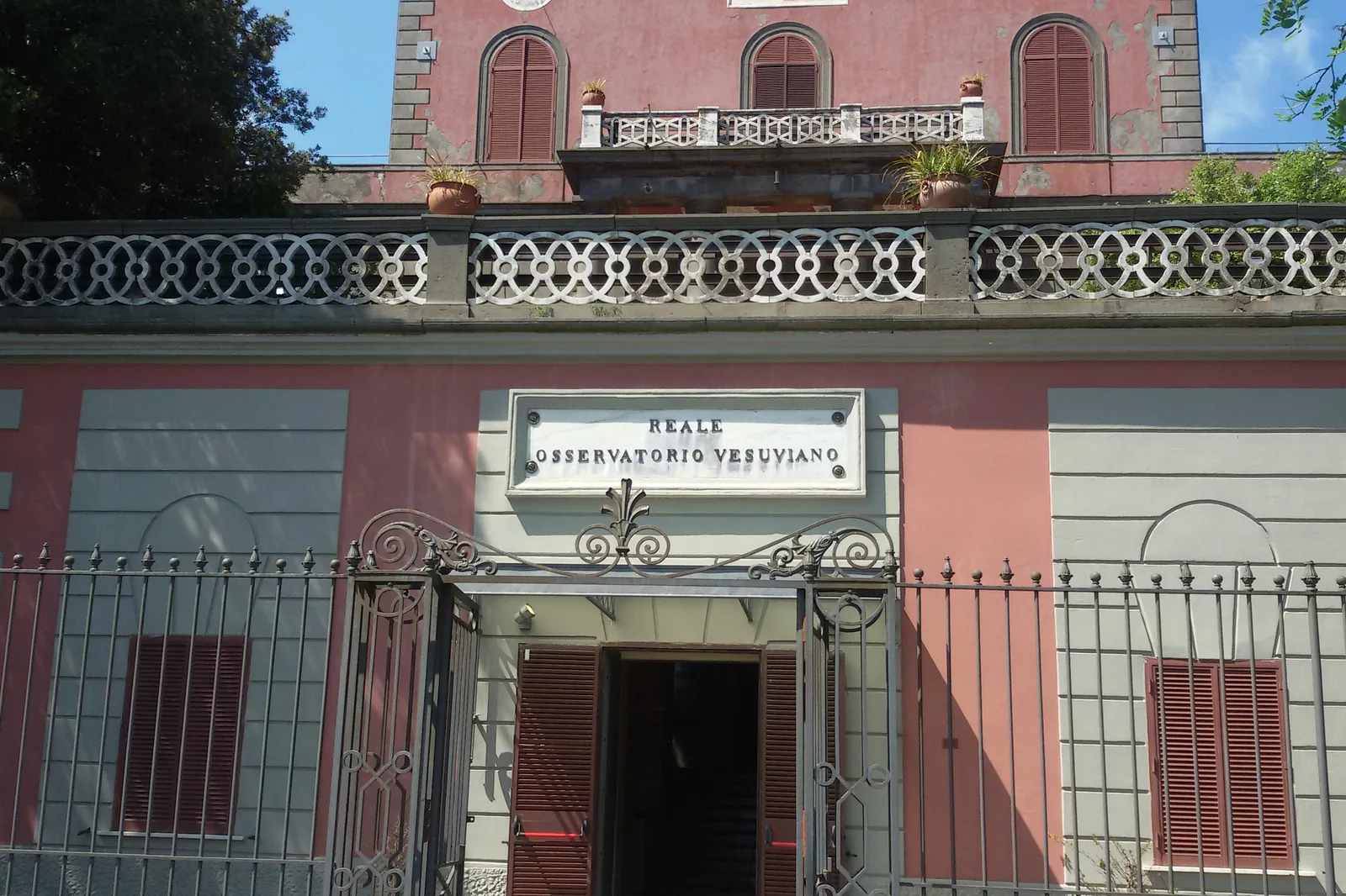 Entrance of the Reale Osservatorio Vesuviano in Vesuvius National Park, with a pink facade and wrought-iron gate
