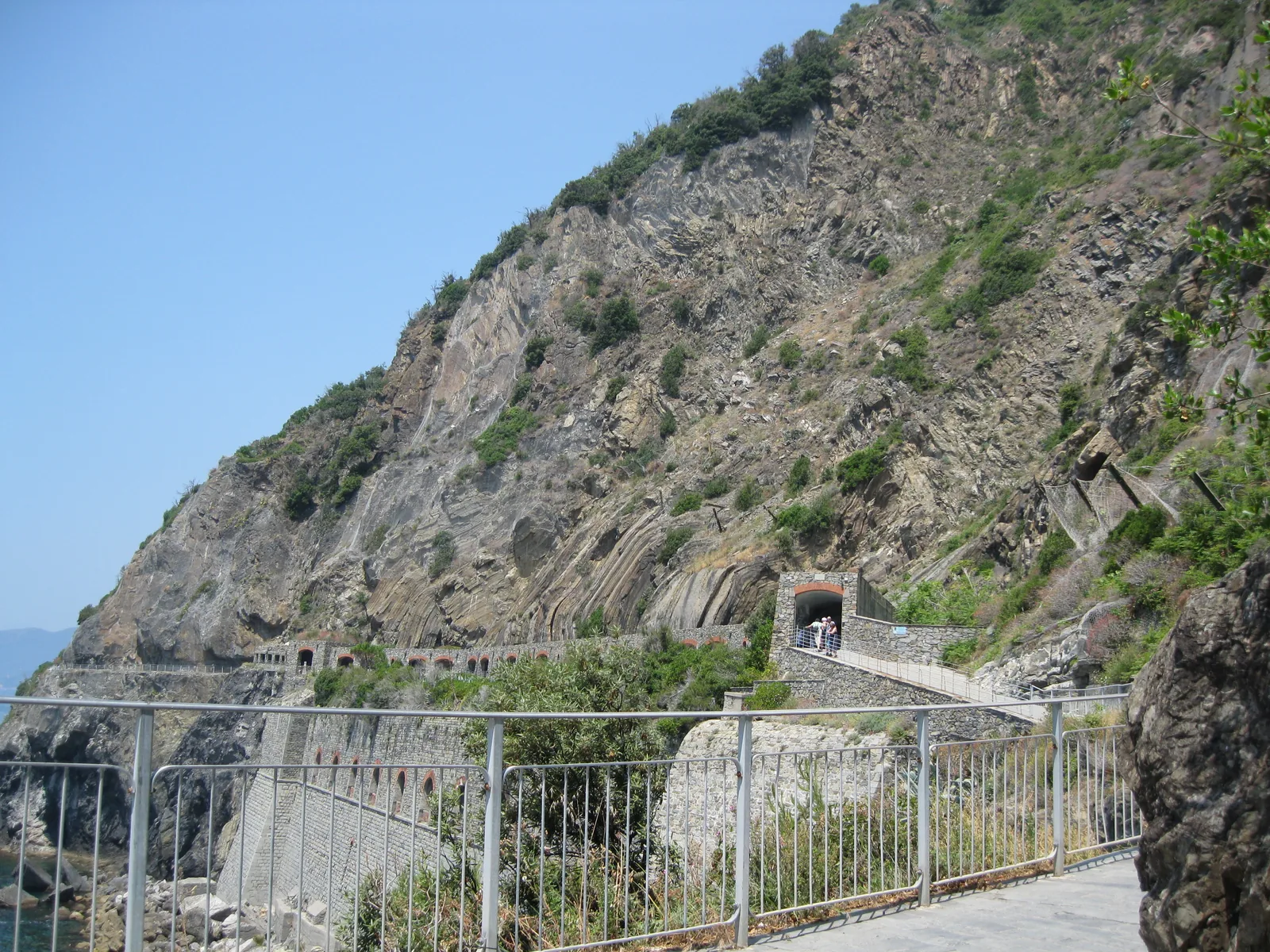 The Via dell'Amore runs with a railing over a railway gallery on the cliff coast near Riomaggiore, with a steep slope of maquis above