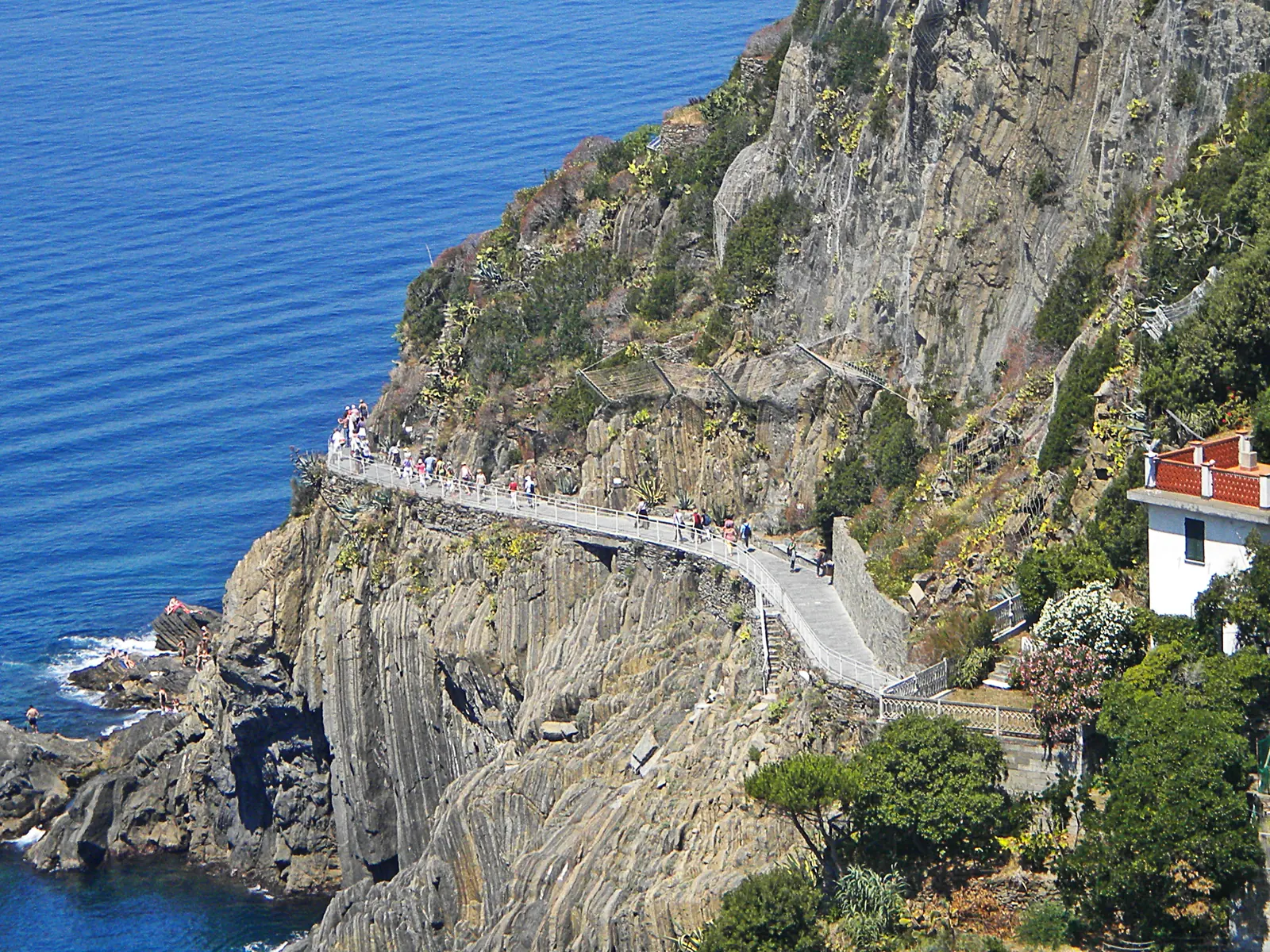 The Via dell'Amore between Riomaggiore and Manarola: a pale path with a railing on the steep cliff coast, deep blue sea below
