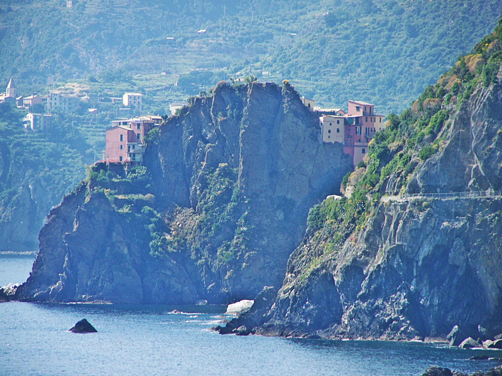 Manarola on a rocky promontory above the sea, with the line of the Via dell'Amore from Riomaggiore on the cliff to the right