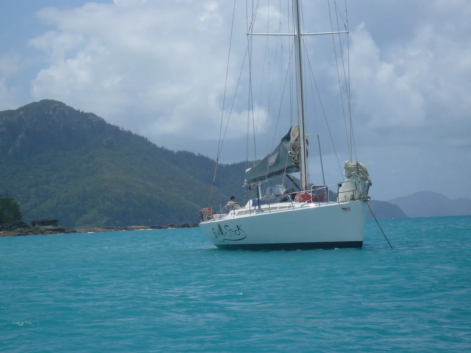 A sailing yacht at anchor in a bay of the Whitsunday Islands on the Great Barrier Reef, forested hills behind