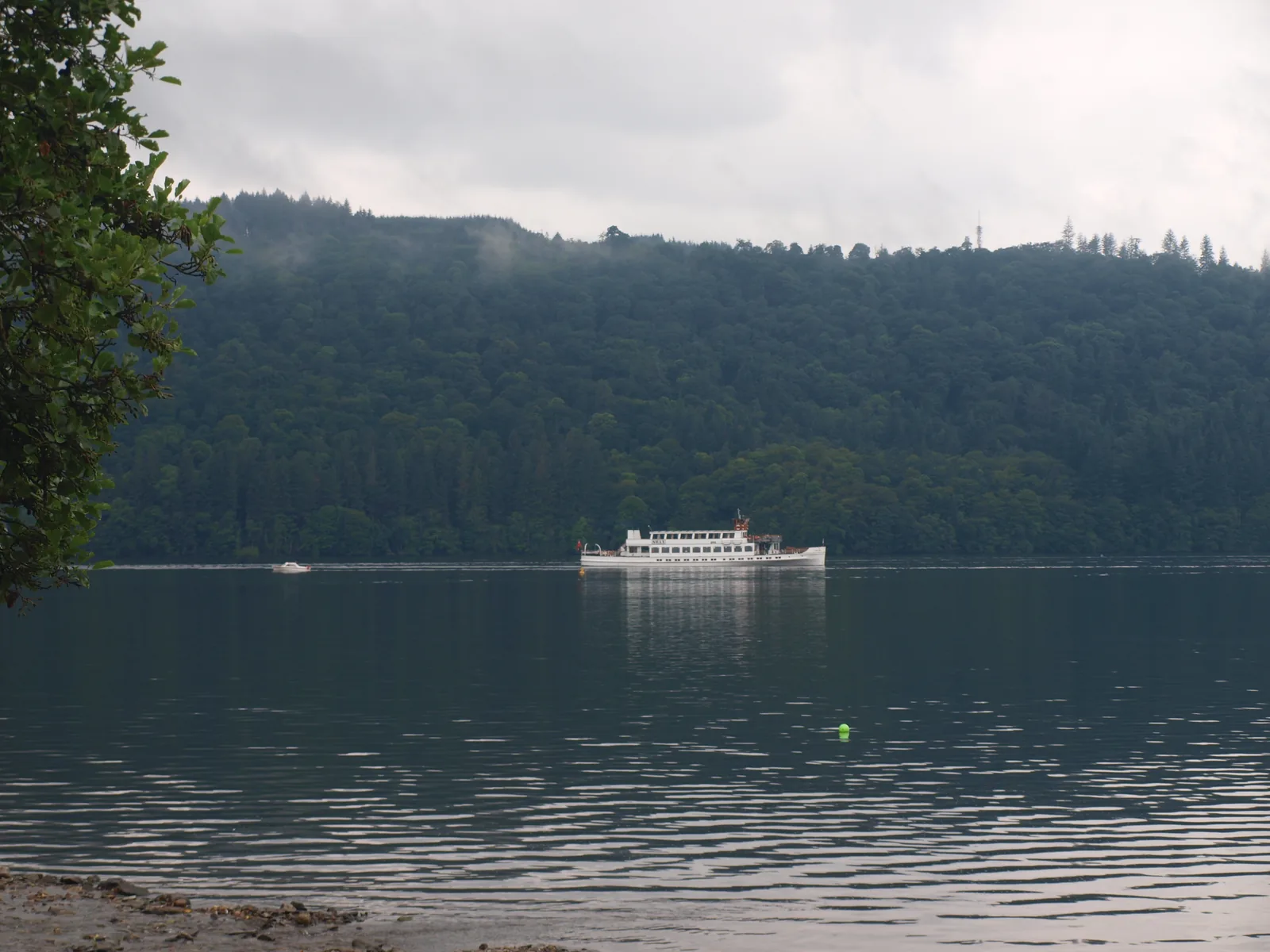 A cruise boat on Windermere in front of the wooded west shore, seen from the shore at Bowness-on-Windermere