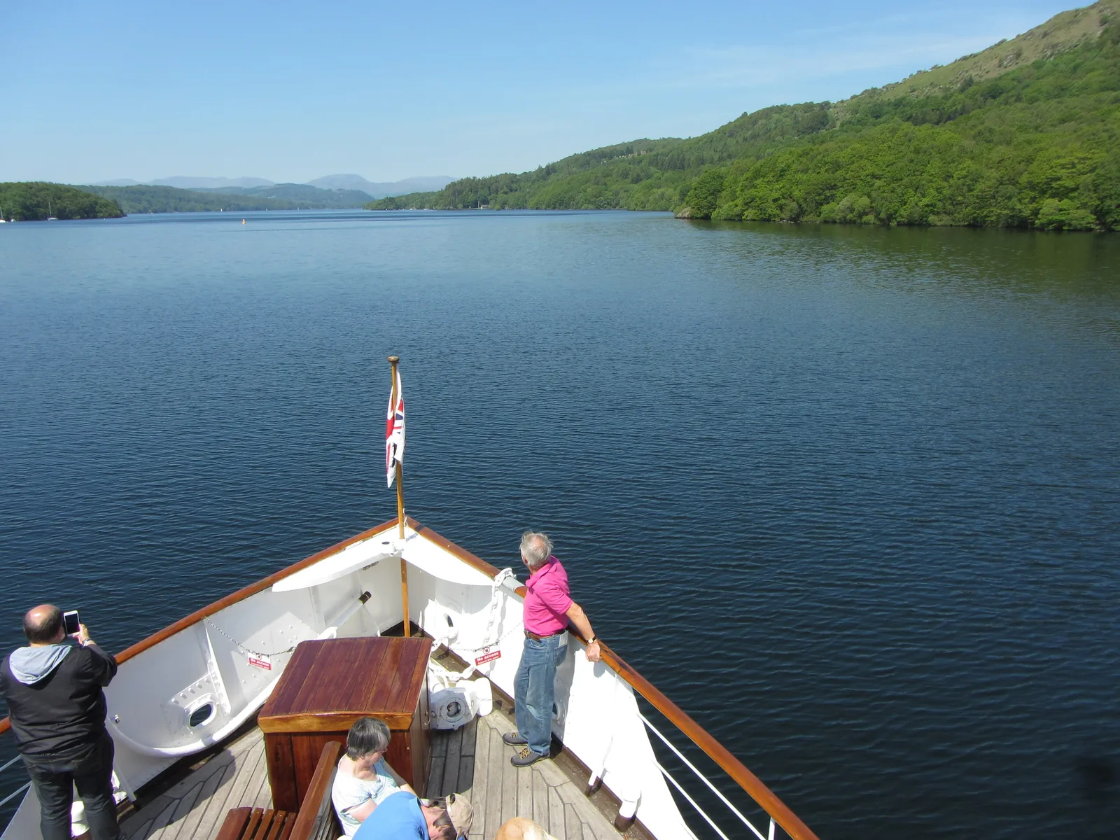 Passengers at the bow of a cruise boat on Windermere in the Lake District, the lake and wooded shores ahead